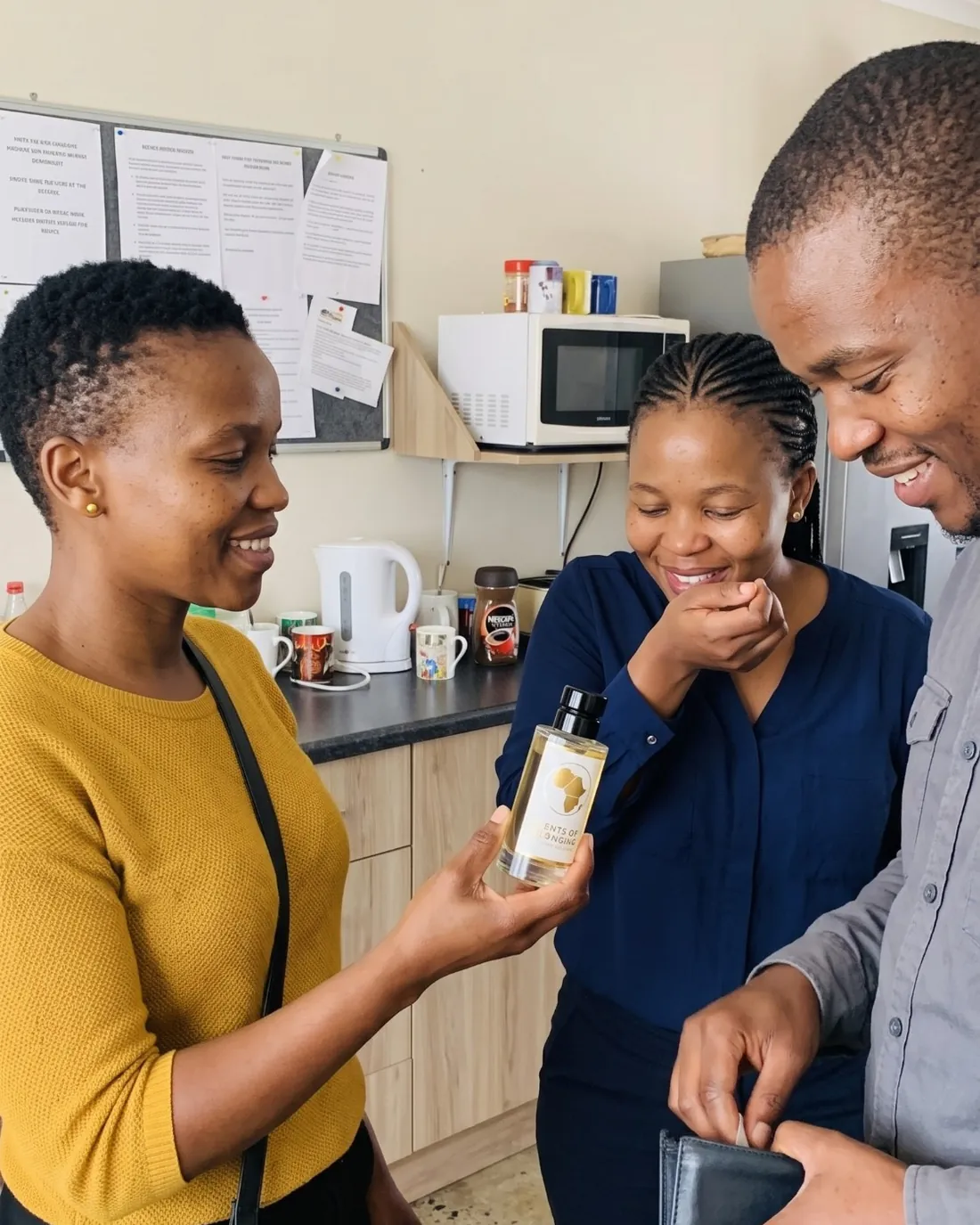 A woman offering a bottle to two colleagues in an office tea room