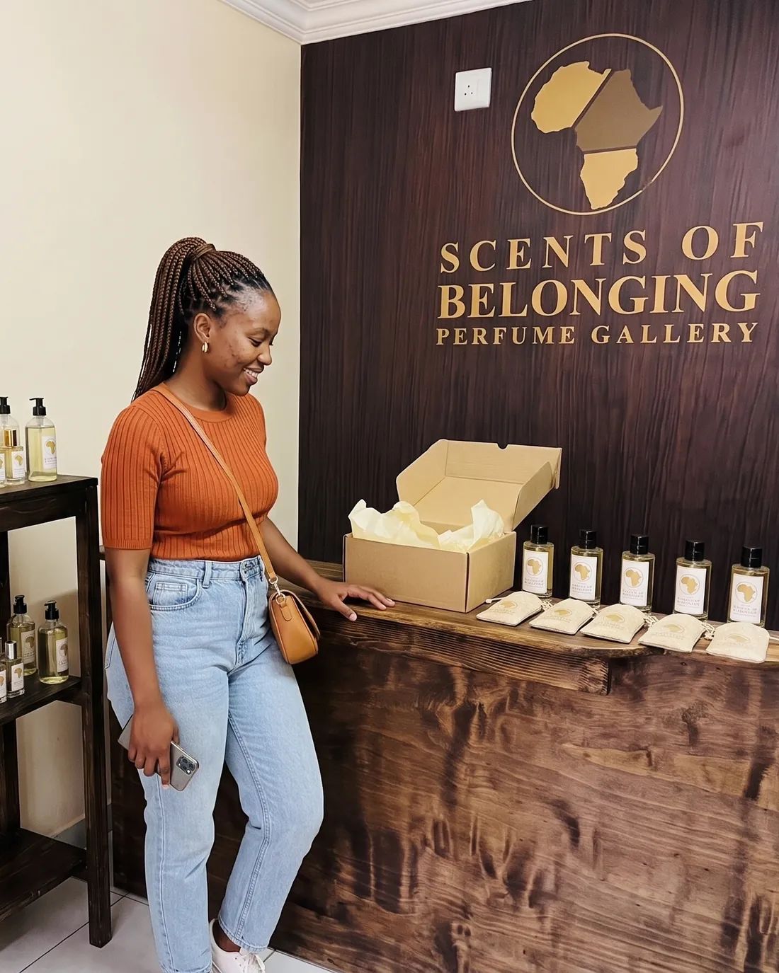 A woman in an orange top at the gallery counter beside her five bottles and the open box