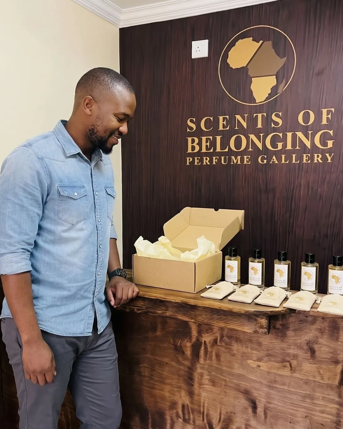 A man in a denim shirt at the gallery counter, smiling at his first five bottles and pouches