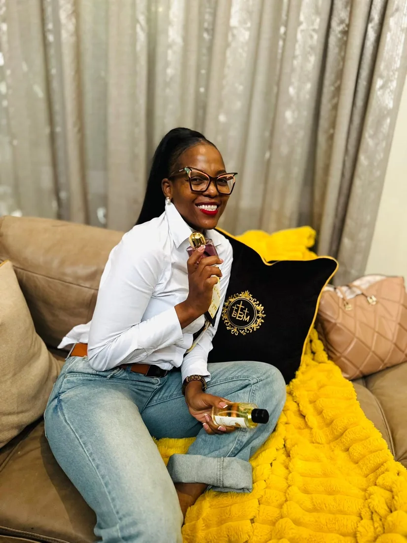 Nthabeleng on her couch, smiling with her gift of perfume