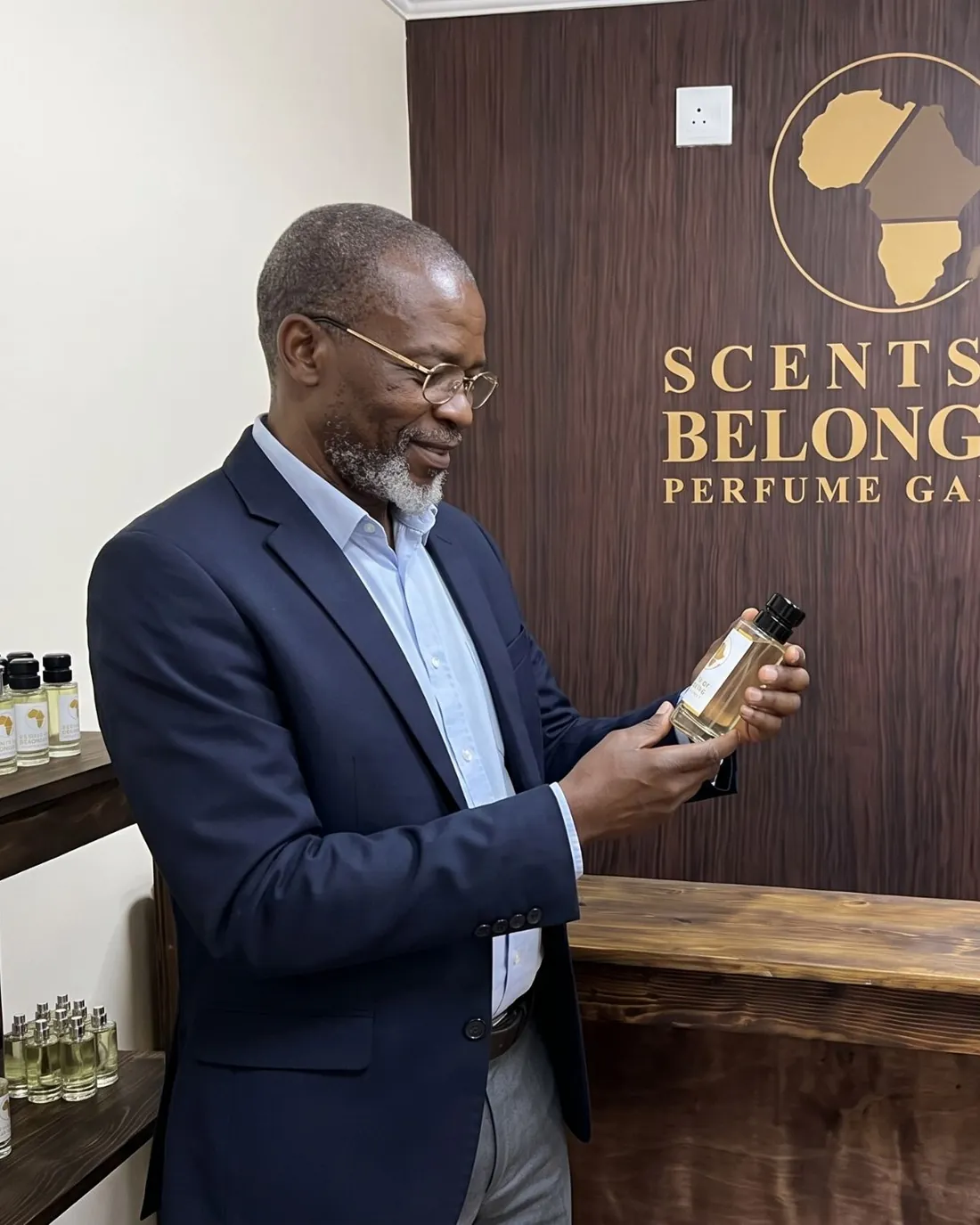 An older man in a navy blazer reading a bottle's label by the gallery's crest wall