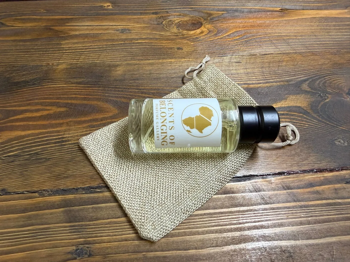 A Scents of Belonging bottle resting on its linen pouch on a walnut table
