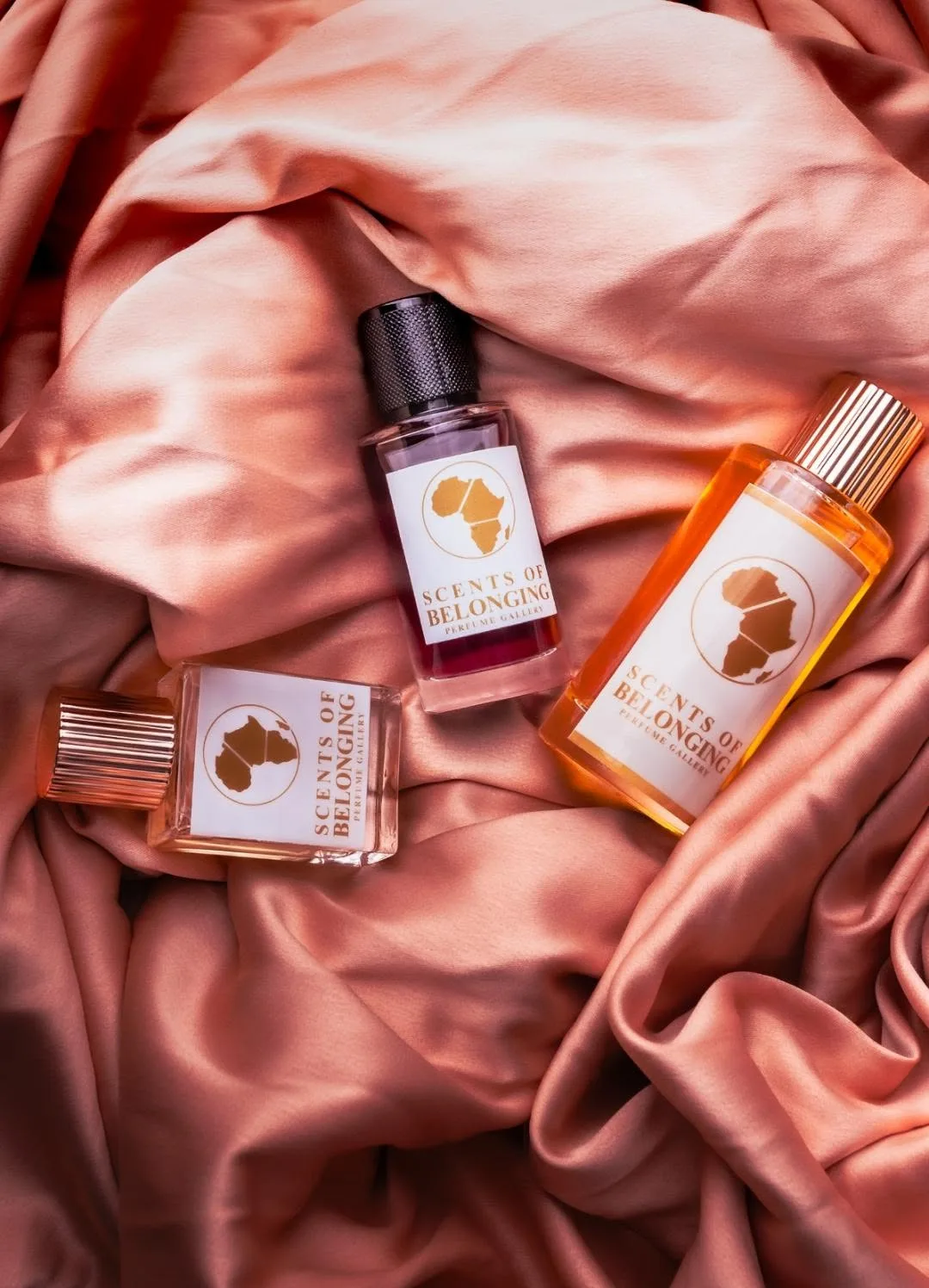 Three Scents of Belonging bottles resting on rose silk